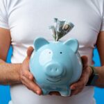 Man holding blue piggy bank with dollar bills sticking out, symbolizing investment savings and financial loss
