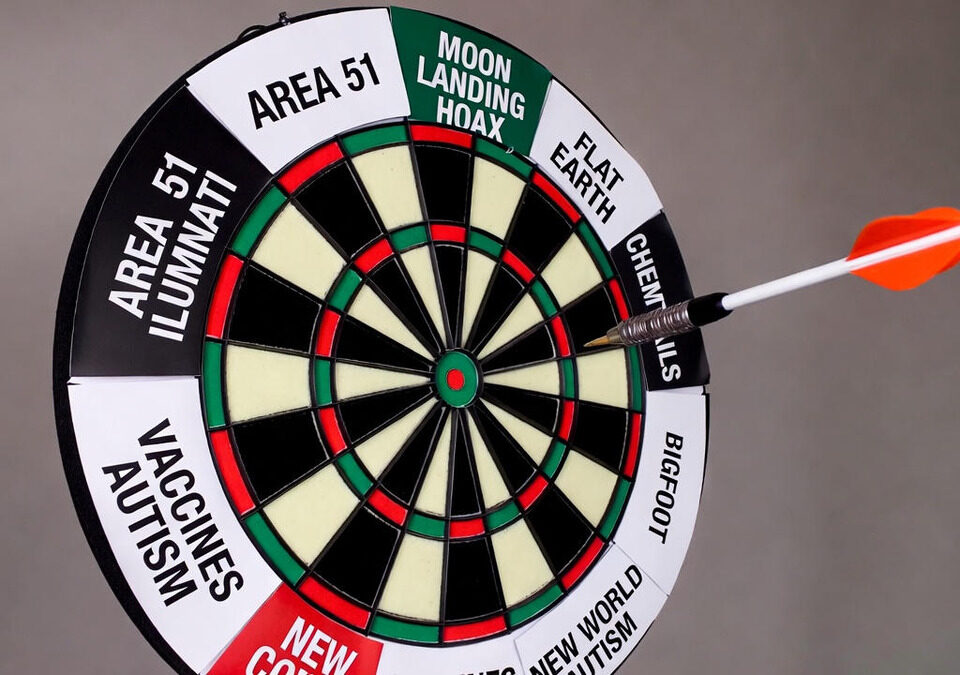 Dartboard labeled with conspiracy theories from AJ Gentile interview, including moon landing hoax and Area 51, with an arrow flying mid-air